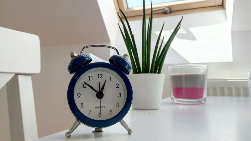 Retro blue alarm clock on a white desk with plant and candle nearby.